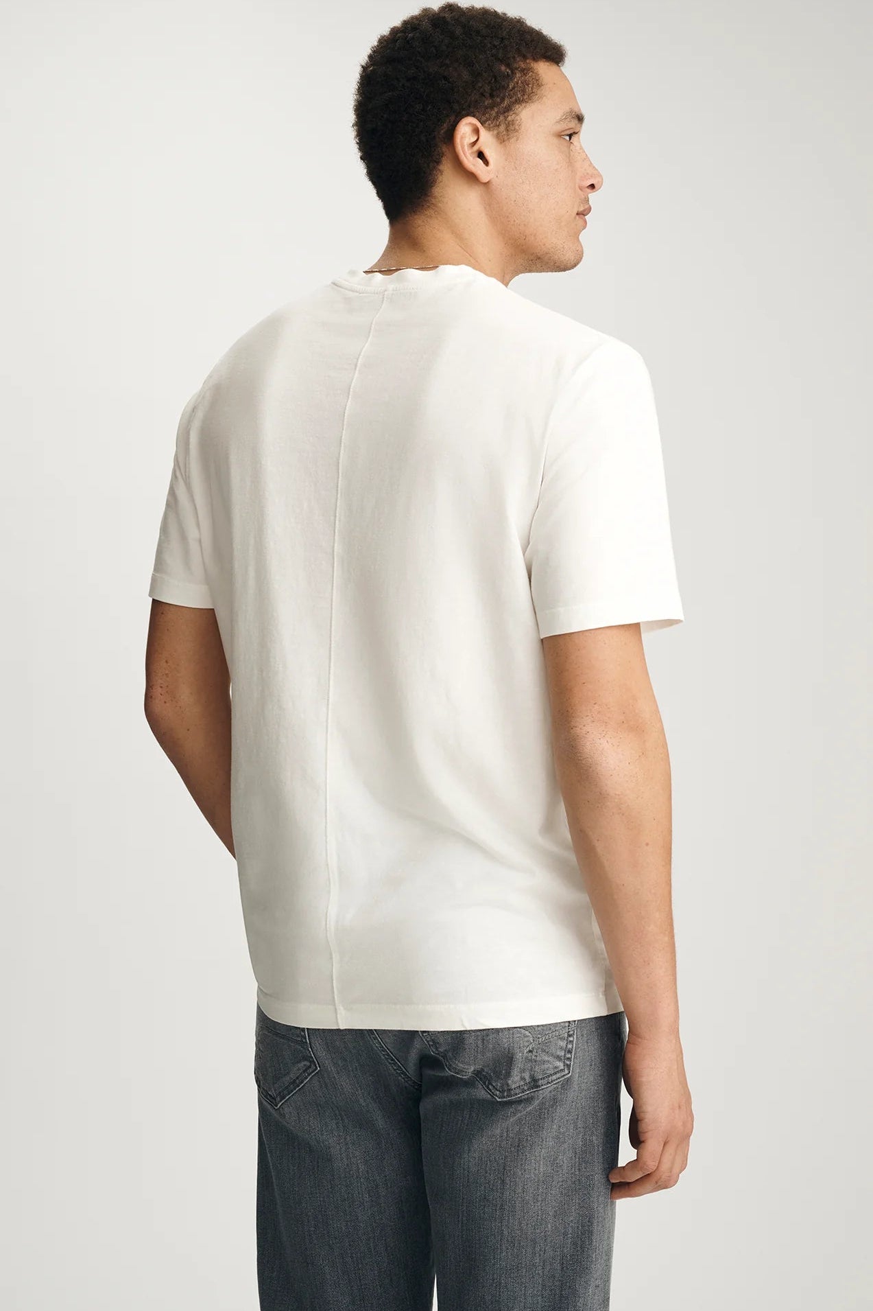 Person wearing a white t-shirt and dark jeans on a light gray background