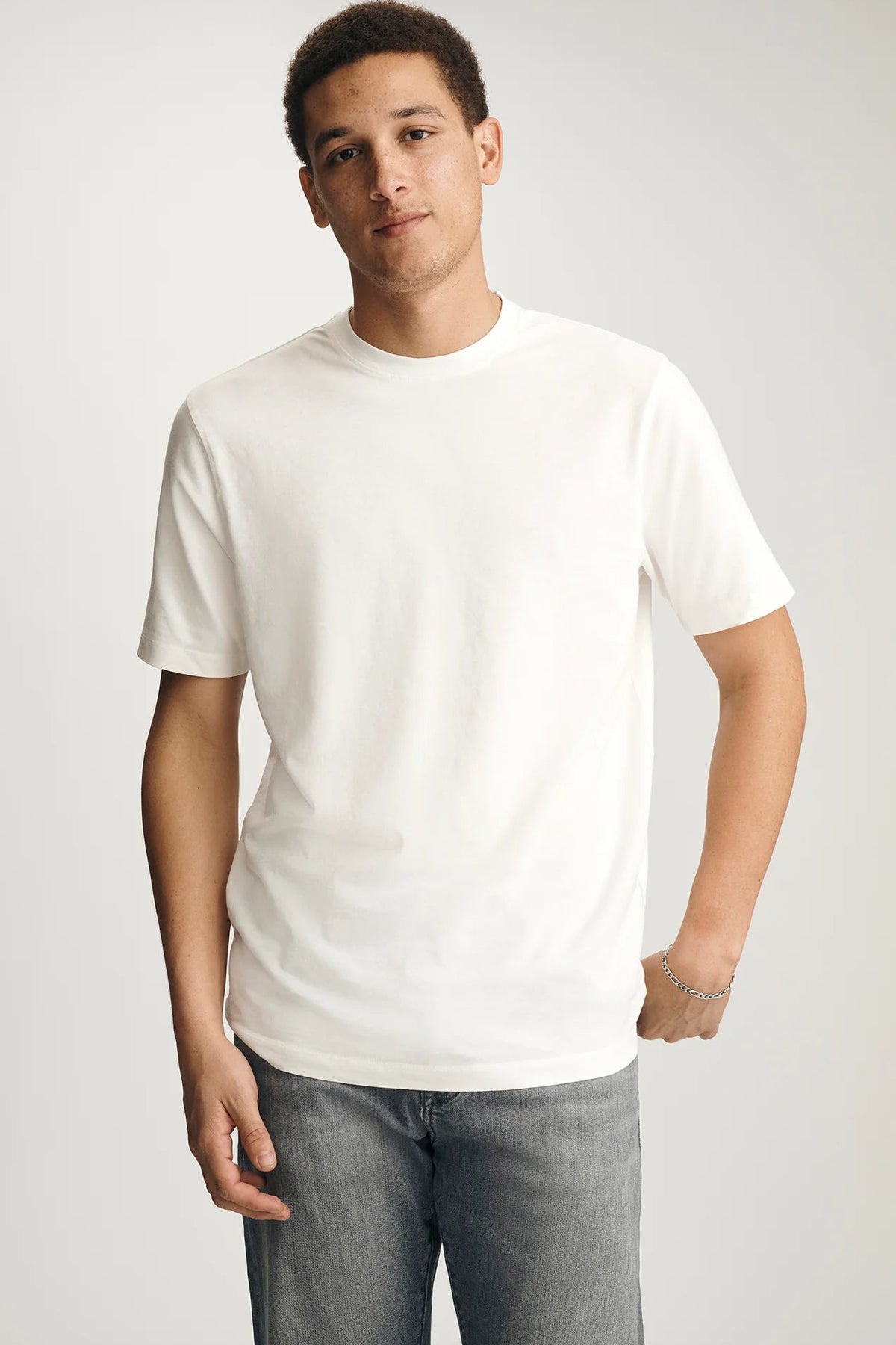 Man wearing a plain white t-shirt and gray jeans against a light gray background