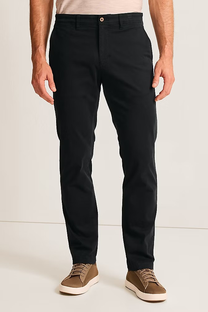 A man wearing slim-fit black chinos with a light beige t-shirt and brown suede sneakers, shown from the waist down against a plain off-white studio background.