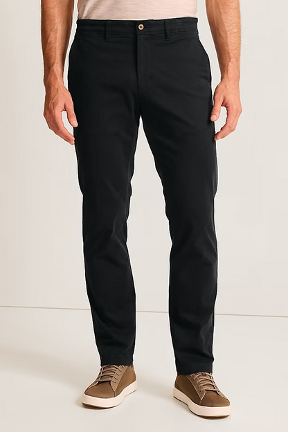 A man wearing slim-fit black chinos with a light beige t-shirt and brown suede sneakers, shown from the waist down against a plain off-white studio background.