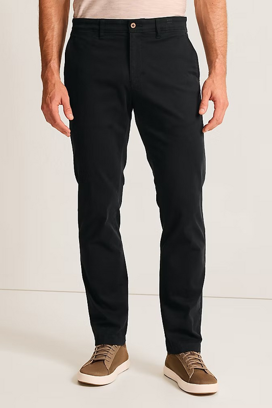 A man wearing slim-fit black chinos with a light beige t-shirt and brown suede sneakers, shown from the waist down against a plain off-white studio background.